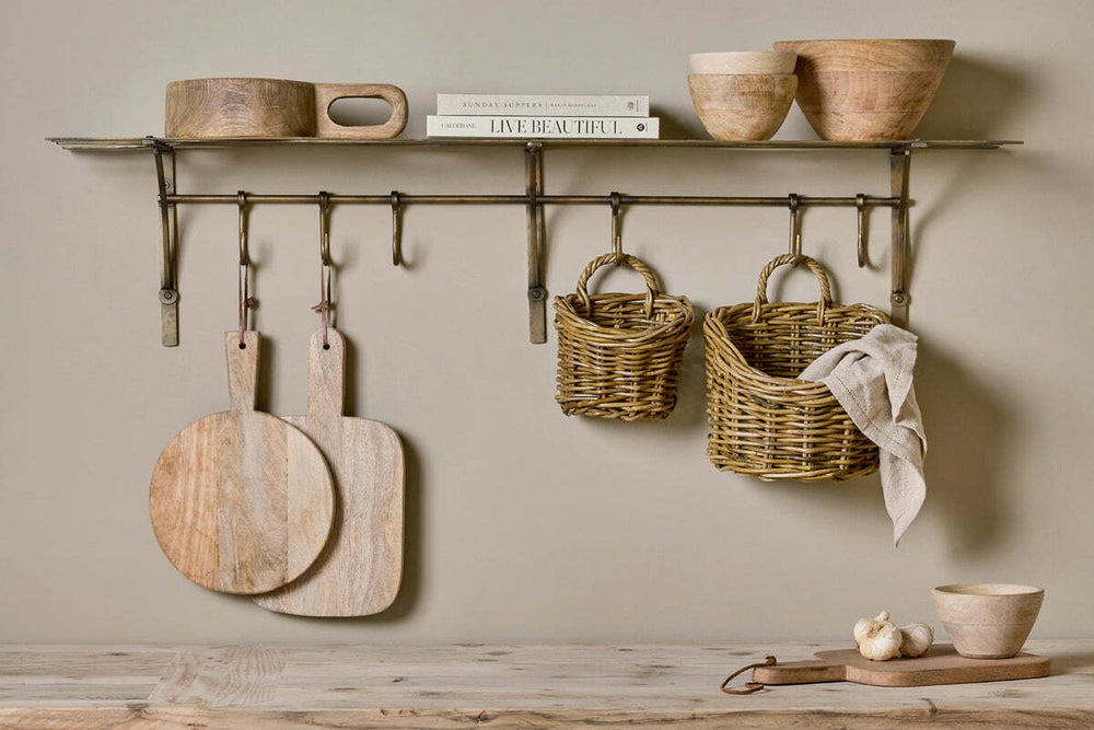 Warm homeware vignette: antique brass shelf with boards and baskets in a hallway
