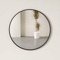 Umbra Hub black round mirror hung on a wall in a dining space